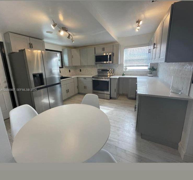 A kitchen features gray cabinetry, stainless steel appliances, white countertops, and a round dining table — 311 NW 32nd Ct, Miami FL 33125, MIAMI, FL