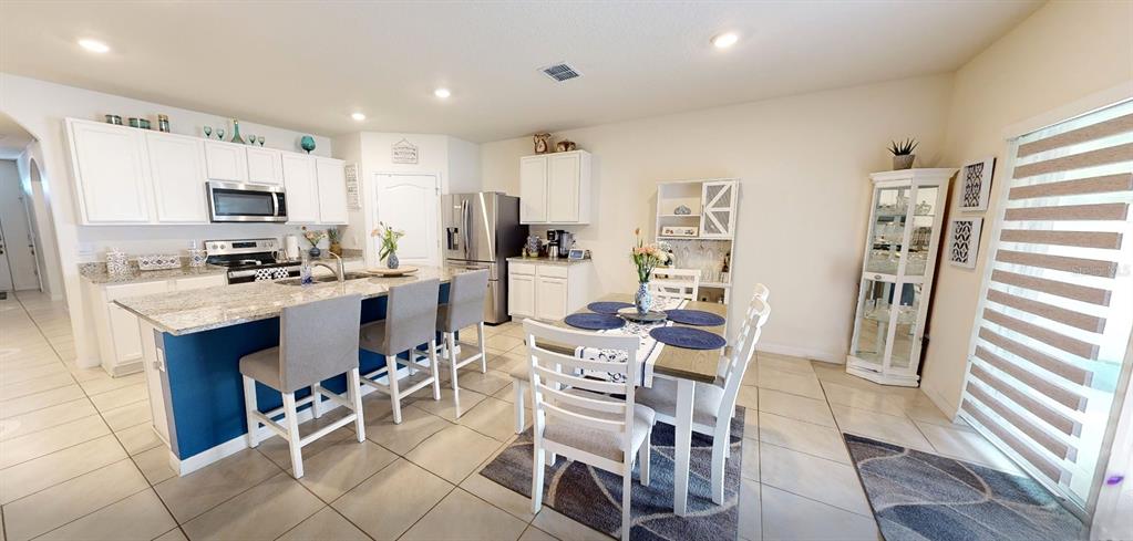 A kitchen and dining area features white cabinets, granite countertops, and a blue island — 5406 PINE LILLY DR, ST CLOUD, FL