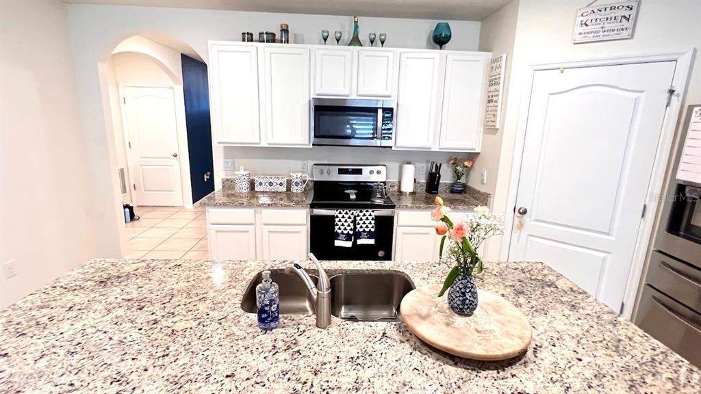 A kitchen features white cabinets, granite countertops, a stainless steel sink, and a black stove — 5406 PINE LILLY DR, ST CLOUD, FL