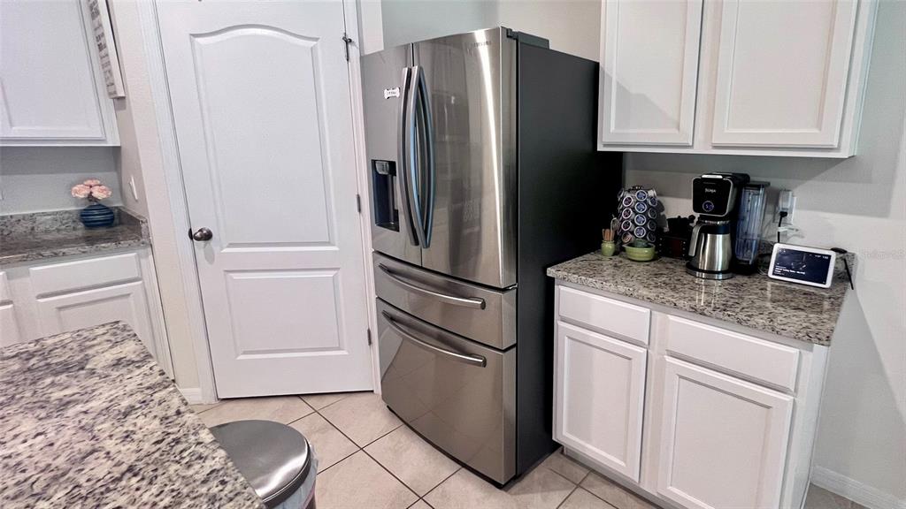 A kitchen features a stainless steel refrigerator, white cabinets, and granite countertops — 5406 PINE LILLY DR, ST CLOUD, FL