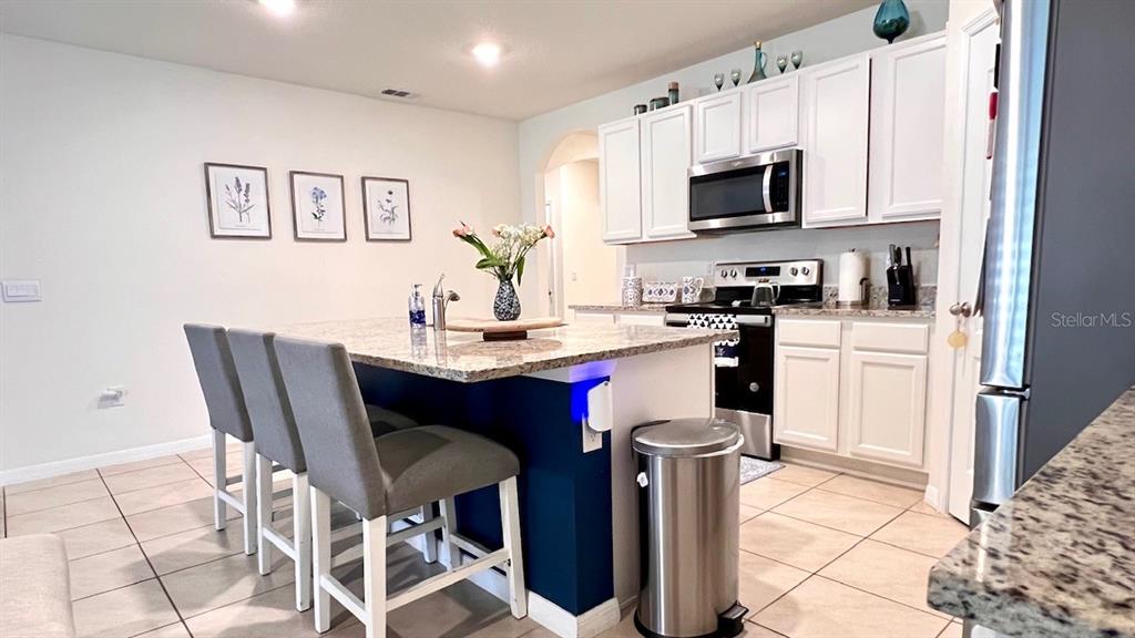 A kitchen features white cabinets, granite countertops, a dark blue island, and three gray stools — 5406 PINE LILLY DR, ST CLOUD, FL