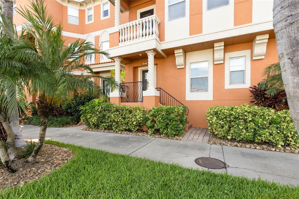 An exterior view of a multi-story orange townhouse with a balcony and landscaped front yard — 905 VILLA VENICIA WAY, TAMPA, FL