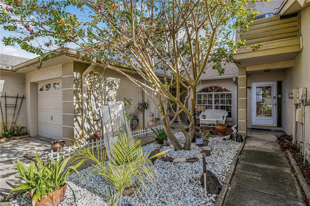 A view of a house exterior featuring a white garage, a gravel garden, and a walkway — 2586 PINE COVE LANE, CLEARWATER, FL