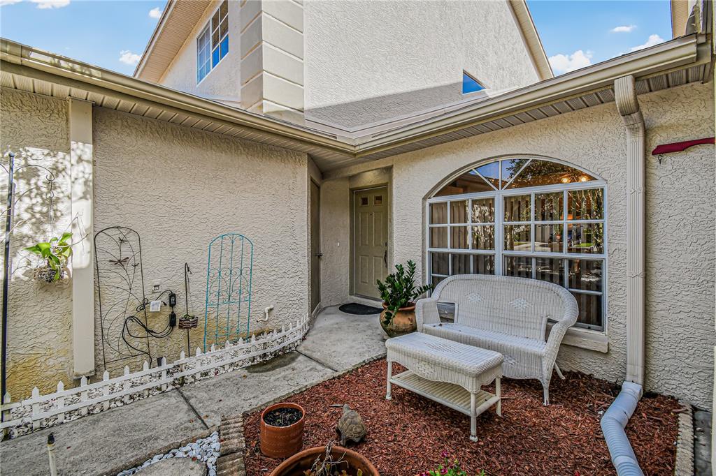 A beige stucco house exterior features a small courtyard with a white wicker bench set — 2586 PINE COVE LANE, CLEARWATER, FL