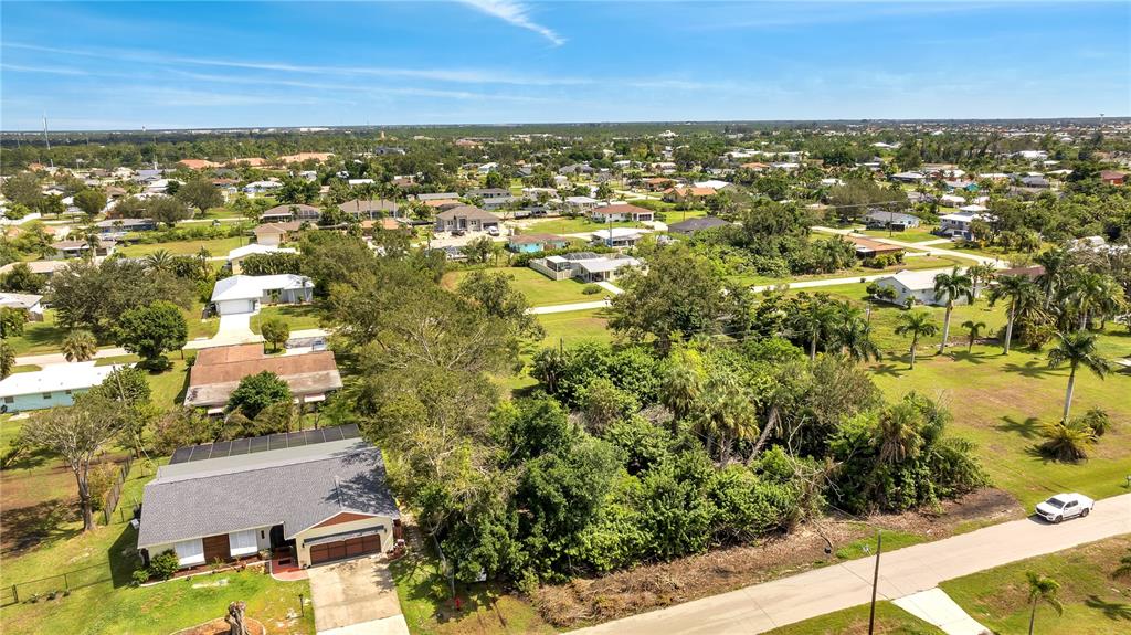 An aerial view shows a suburban neighborhood with houses, trees, and a paved road — 2720 POINCIANA COURT, PUNTA GORDA, FL