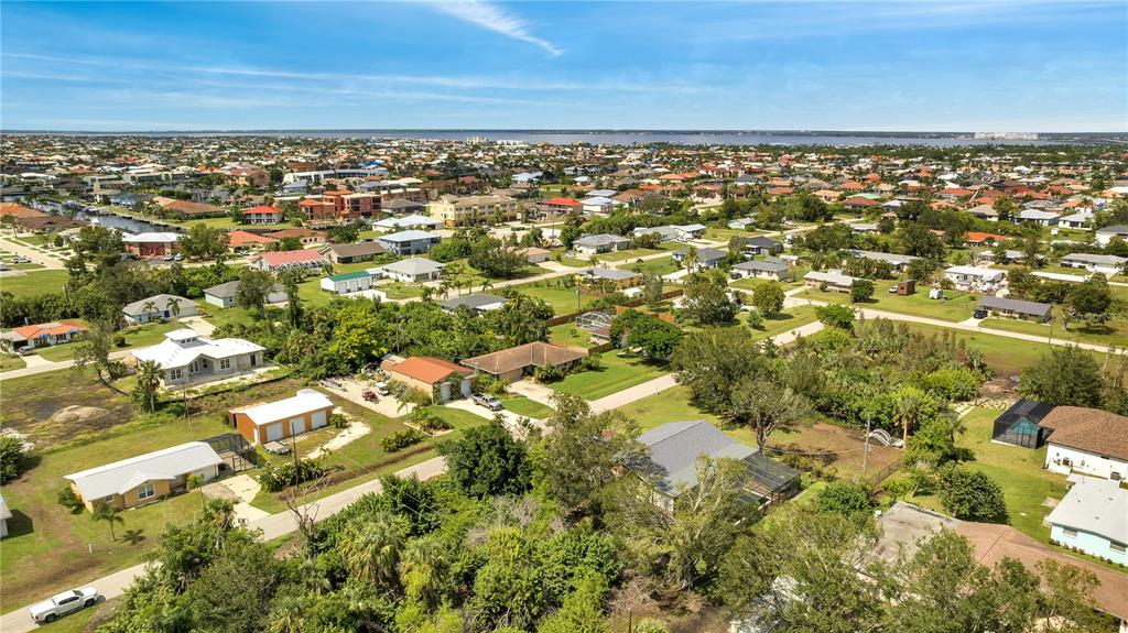 An aerial view shows a suburban neighborhood with single-family homes, lush trees, and distant water — 2720 POINCIANA COURT, PUNTA GORDA, FL