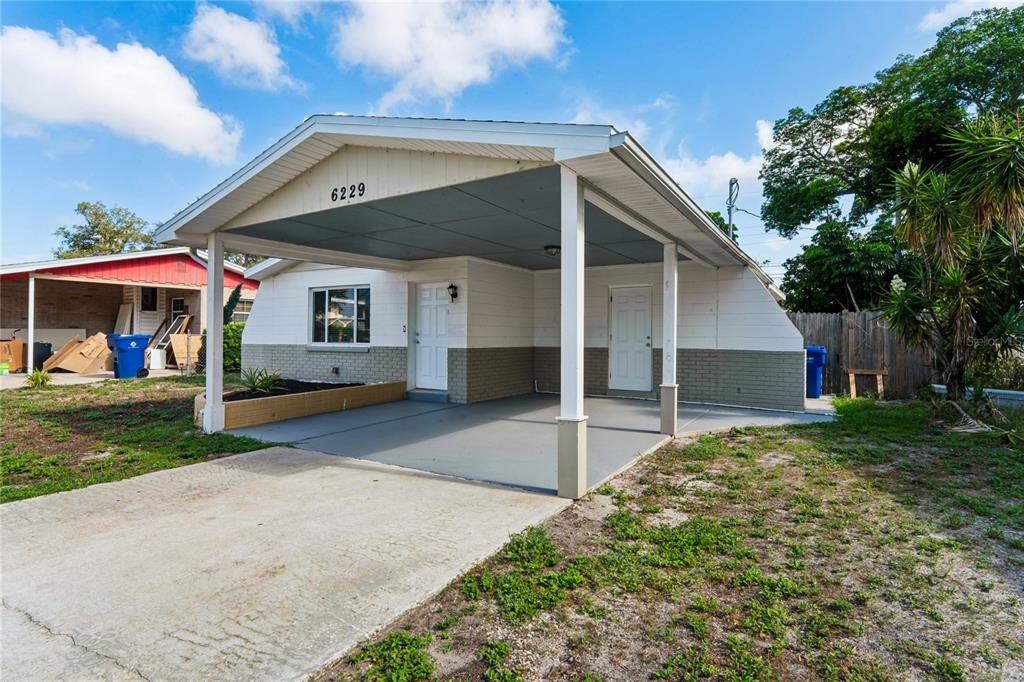 A single-story house exterior features a covered carport, white siding, and a concrete driveway — 6229 50TH AVENUE N, ST PETERSBURG, FL