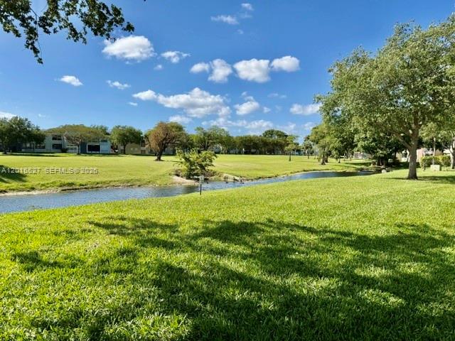 A grassy lawn slopes down to a narrow canal with trees and buildings in the background — 7396 NW 18th St # 101, Margate FL 33063, MARGATE, FL