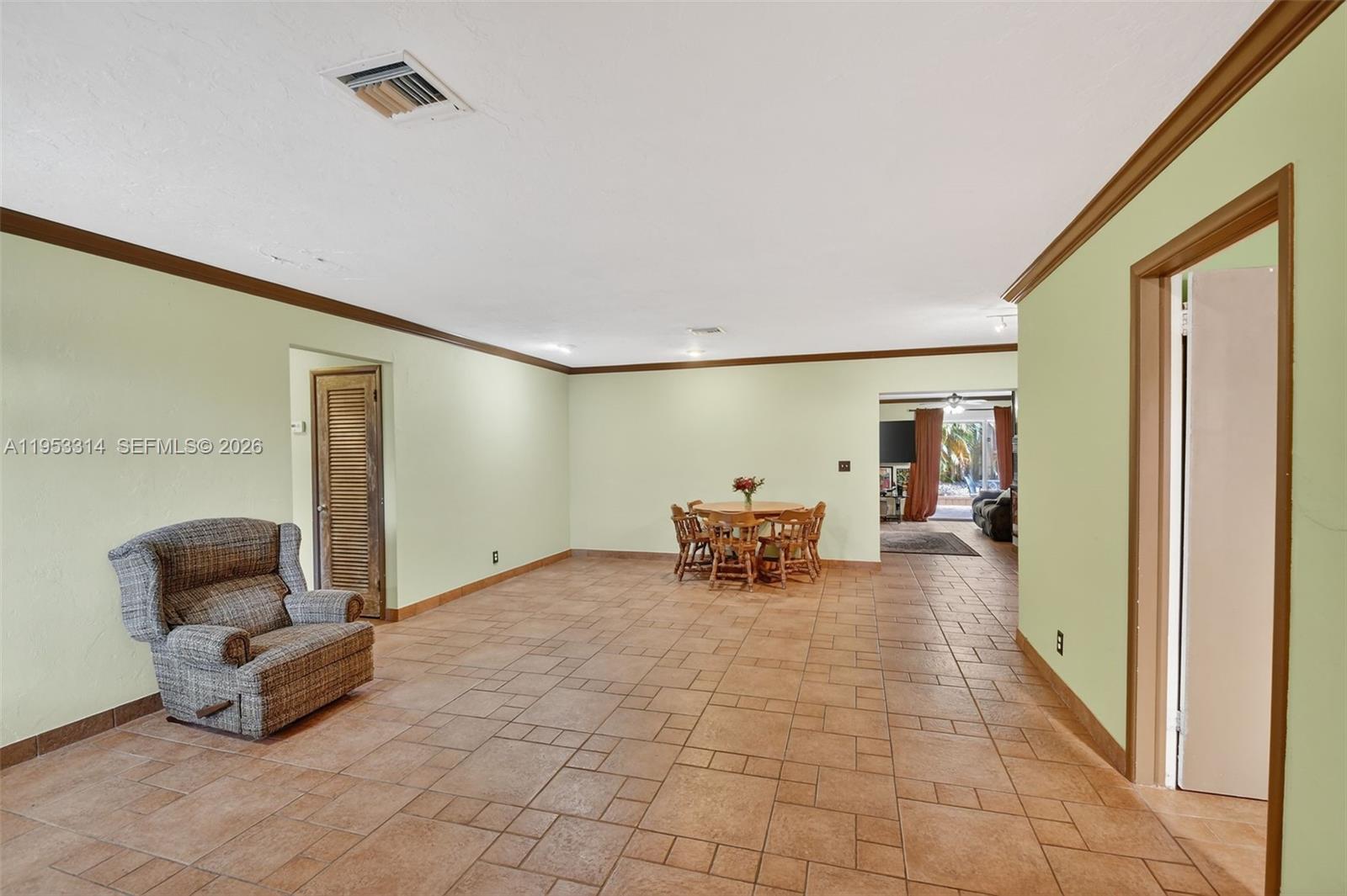 A spacious room with light green walls, brown trim, and tiled flooring features a dining set — 1712 High Ridge Rd, Lake Worth FL 33461, LAKE WORTH, FL