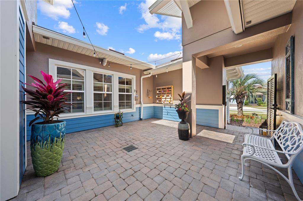A paved outdoor courtyard features blue siding, a white bench, and potted plants — 12735 BANTING TERRACE, ORLANDO, FL