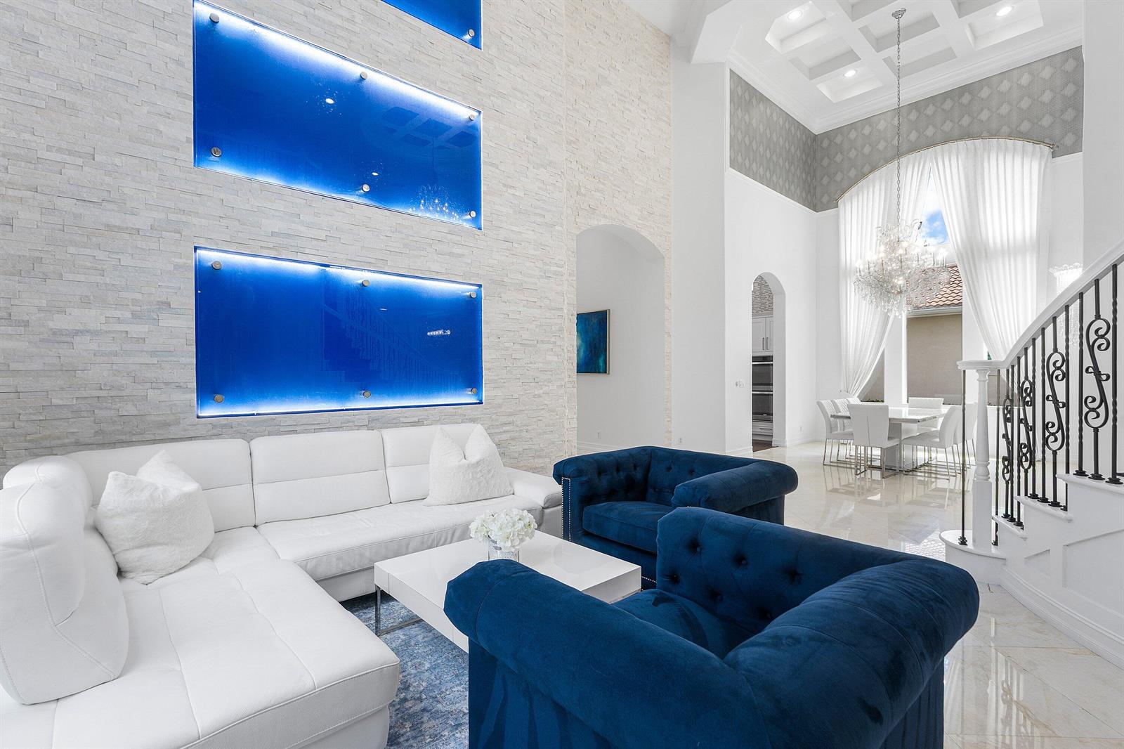 A living room features a white sectional, blue velvet chairs, and illuminated blue wall panels — 131 Carmela Court, Jupiter FL 33478, JUPITER, FL