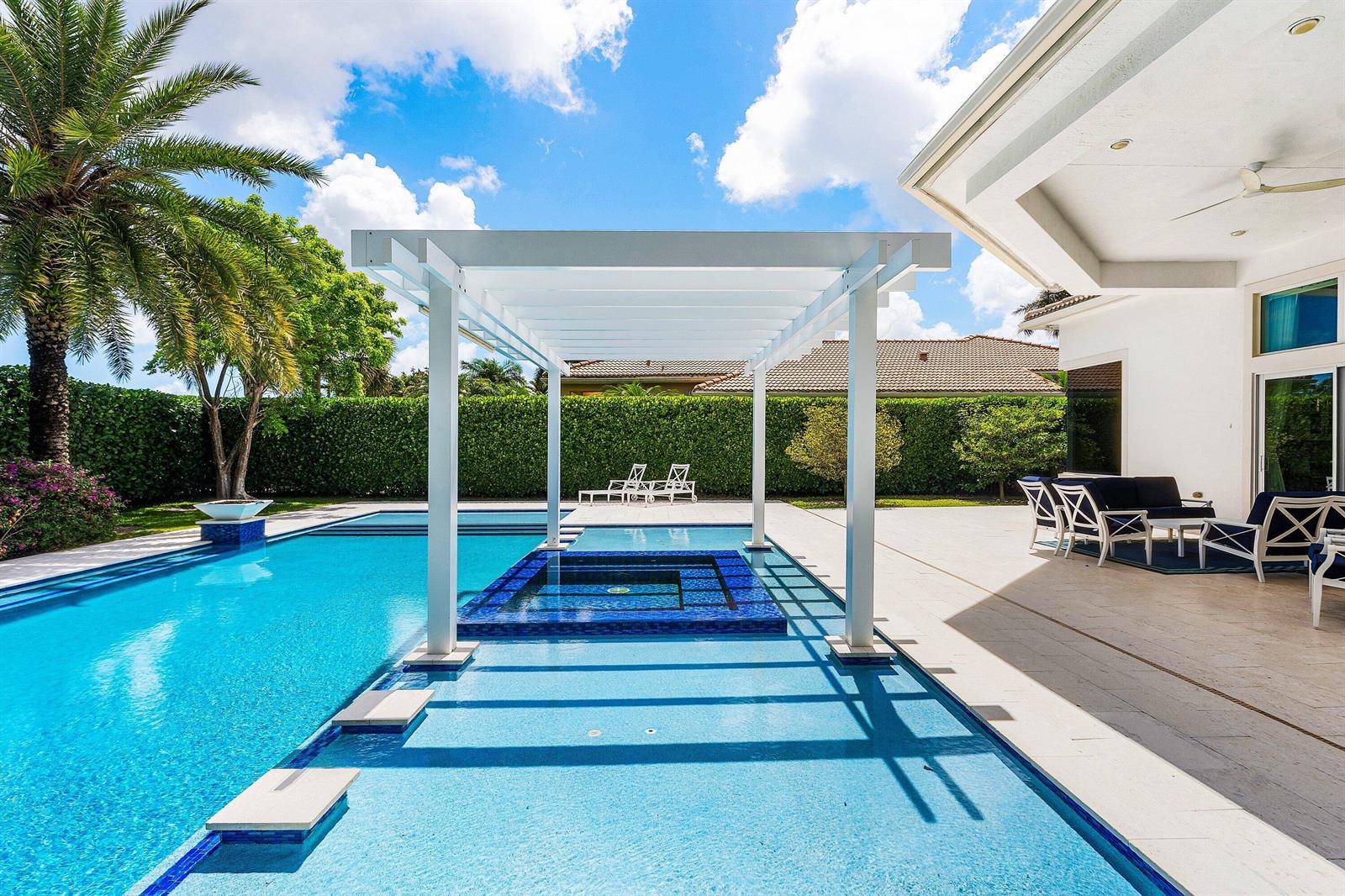 A backyard swimming pool with a central spa, white pergola, and adjacent covered patio area — 131 Carmela Court, Jupiter FL 33478, JUPITER, FL