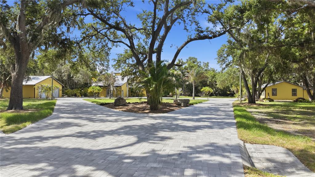 A paved driveway splits in front of yellow buildings surrounded by large, moss-draped oak trees — 3348 ALAMO LANE, SARASOTA, FL