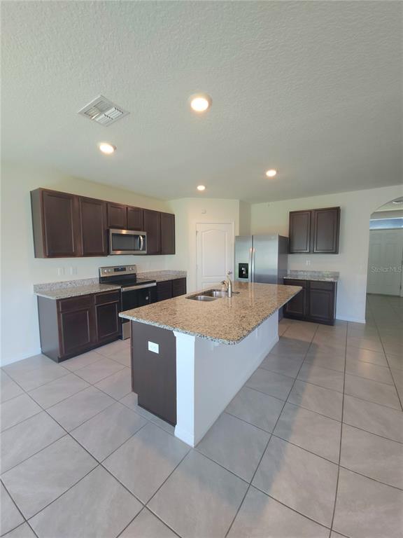 A kitchen features dark wood cabinets, granite countertops, stainless steel appliances, and tile flooring — 575 TORTUGAS STREET, HAINES CITY, FL