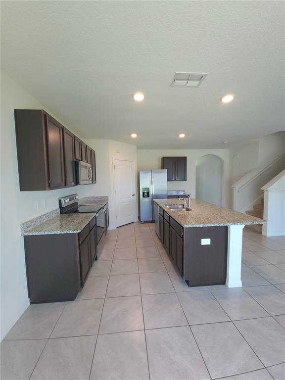 A kitchen features dark brown cabinets, granite countertops, stainless steel appliances, and light tile flooring — 575 TORTUGAS STREET, HAINES CITY, FL
