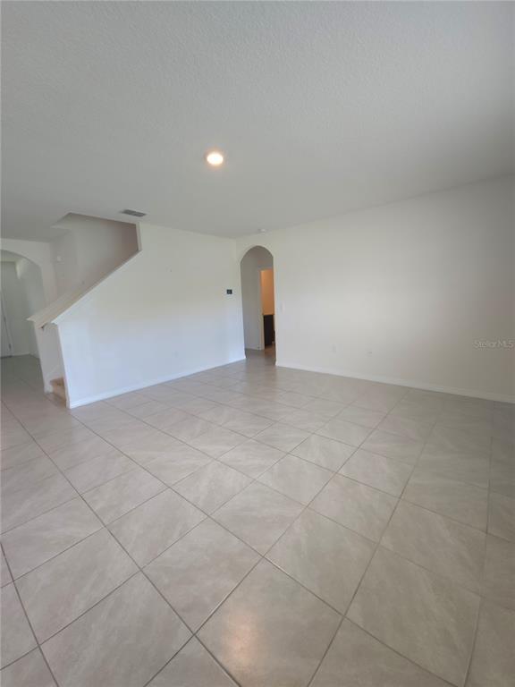 A spacious room with light-colored tile flooring, white walls, and a staircase — 575 TORTUGAS STREET, HAINES CITY, FL