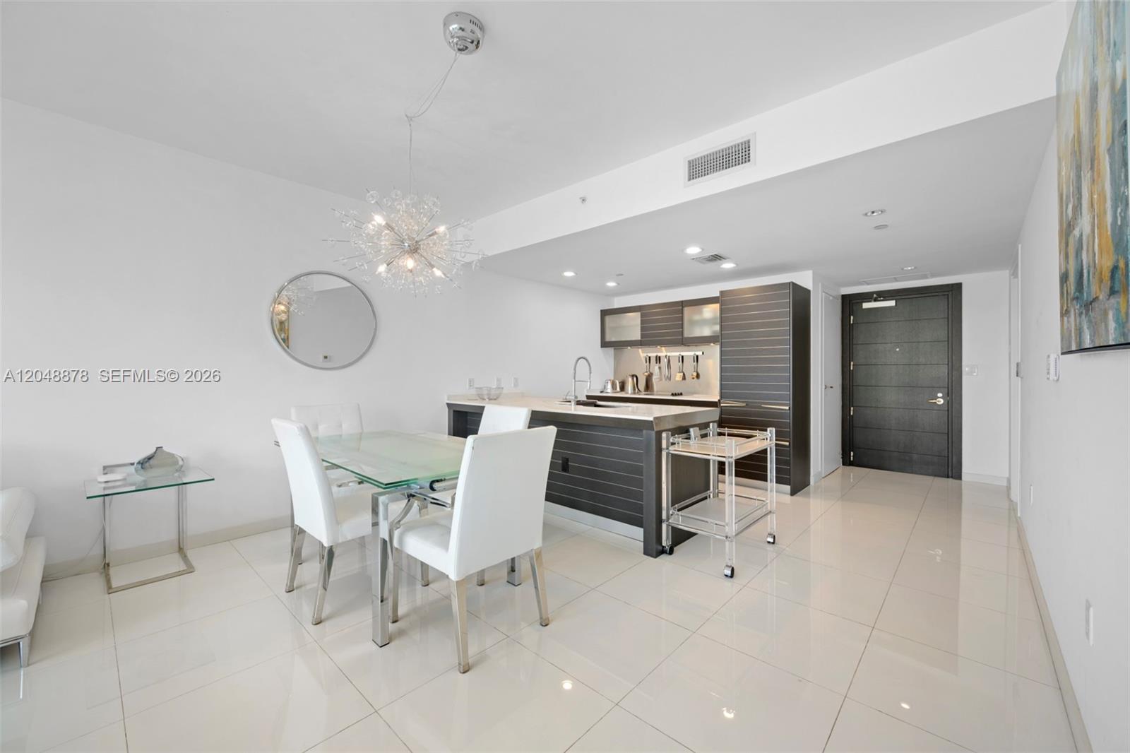 A modern kitchen and dining area feature white tile floors, dark cabinetry, and glass furniture — 200 Biscayne Boulevard Way # 4314, Miami FL 33131, MIAMI, FL