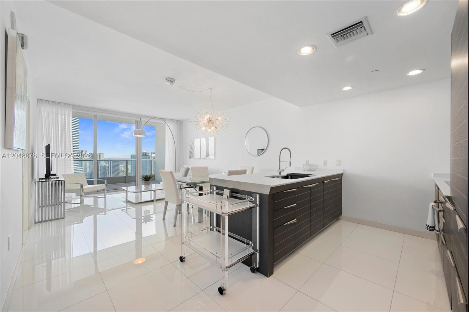 A modern kitchen and living area with white tile floors, dark cabinetry, and floor-to-ceiling windows — 200 Biscayne Boulevard Way # 4314, Miami FL 33131, MIAMI, FL
