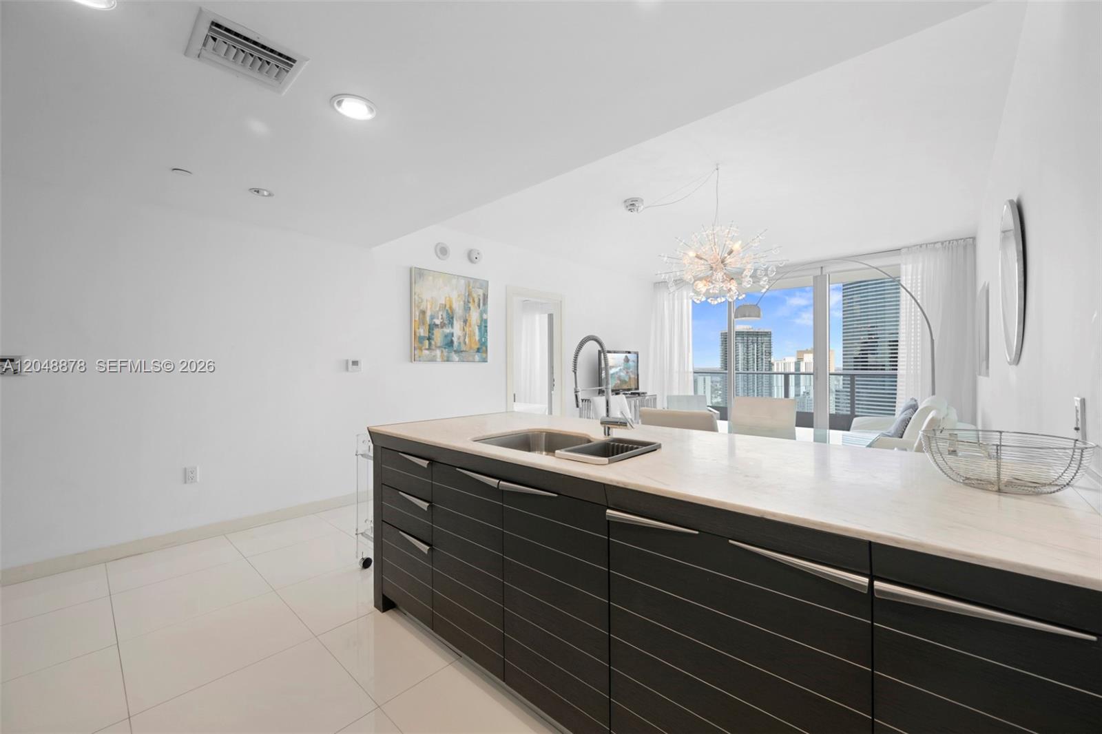 A modern kitchen island with dark wood cabinetry and a light countertop faces a living area — 200 Biscayne Boulevard Way # 4314, Miami FL 33131, MIAMI, FL