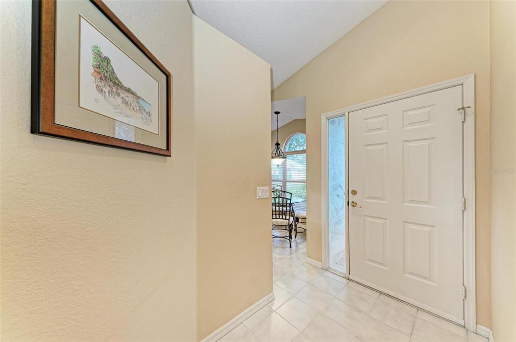 A tiled entryway features a white front door with a glass sidelight and wall art — 4936 LINSEY COURT, SARASOTA, FL