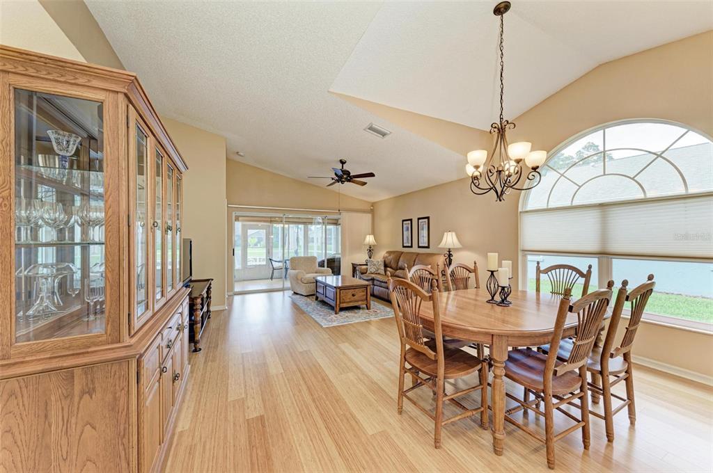 A dining area and living room with wood-look flooring, vaulted ceilings, and a large window — 4936 LINSEY COURT, SARASOTA, FL