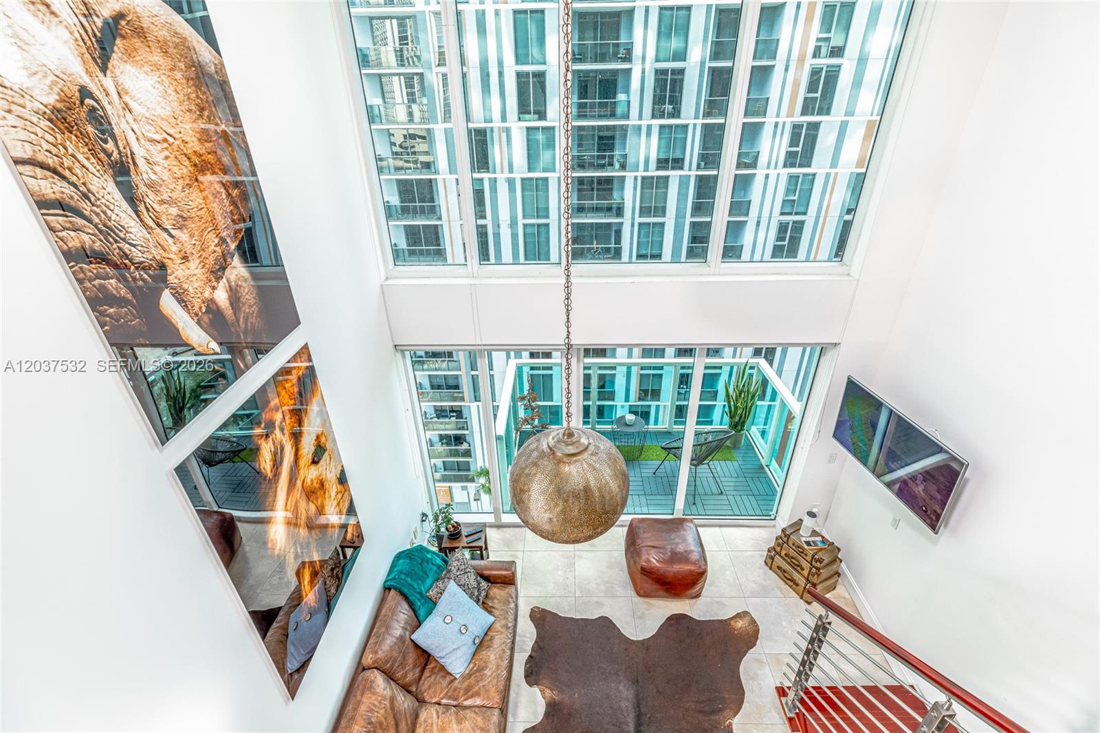 A high-ceiling living room features a leather sofa, a large pendant light, and floor-to-ceiling windows — 41 SE 5th St # 706, Miami FL 33131, MIAMI, FL