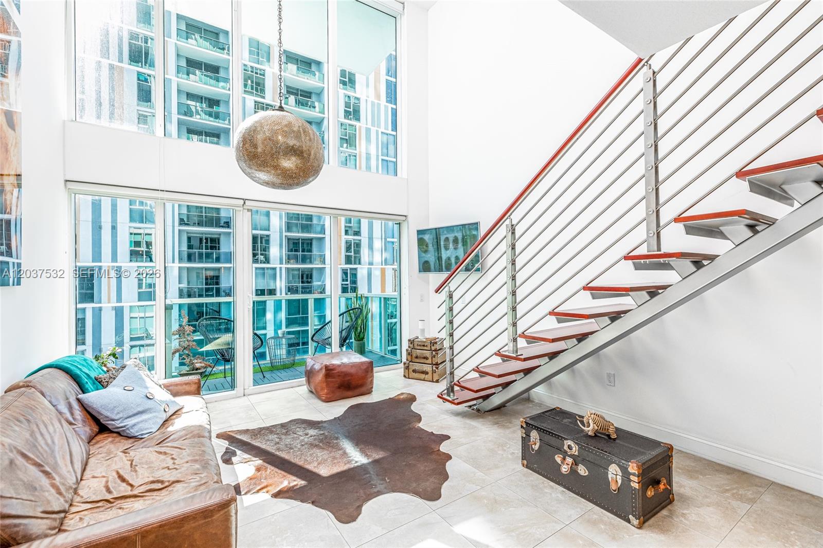 A modern living room features a floating staircase, floor-to-ceiling windows, and a leather sofa — 41 SE 5th St # 706, Miami FL 33131, MIAMI, FL