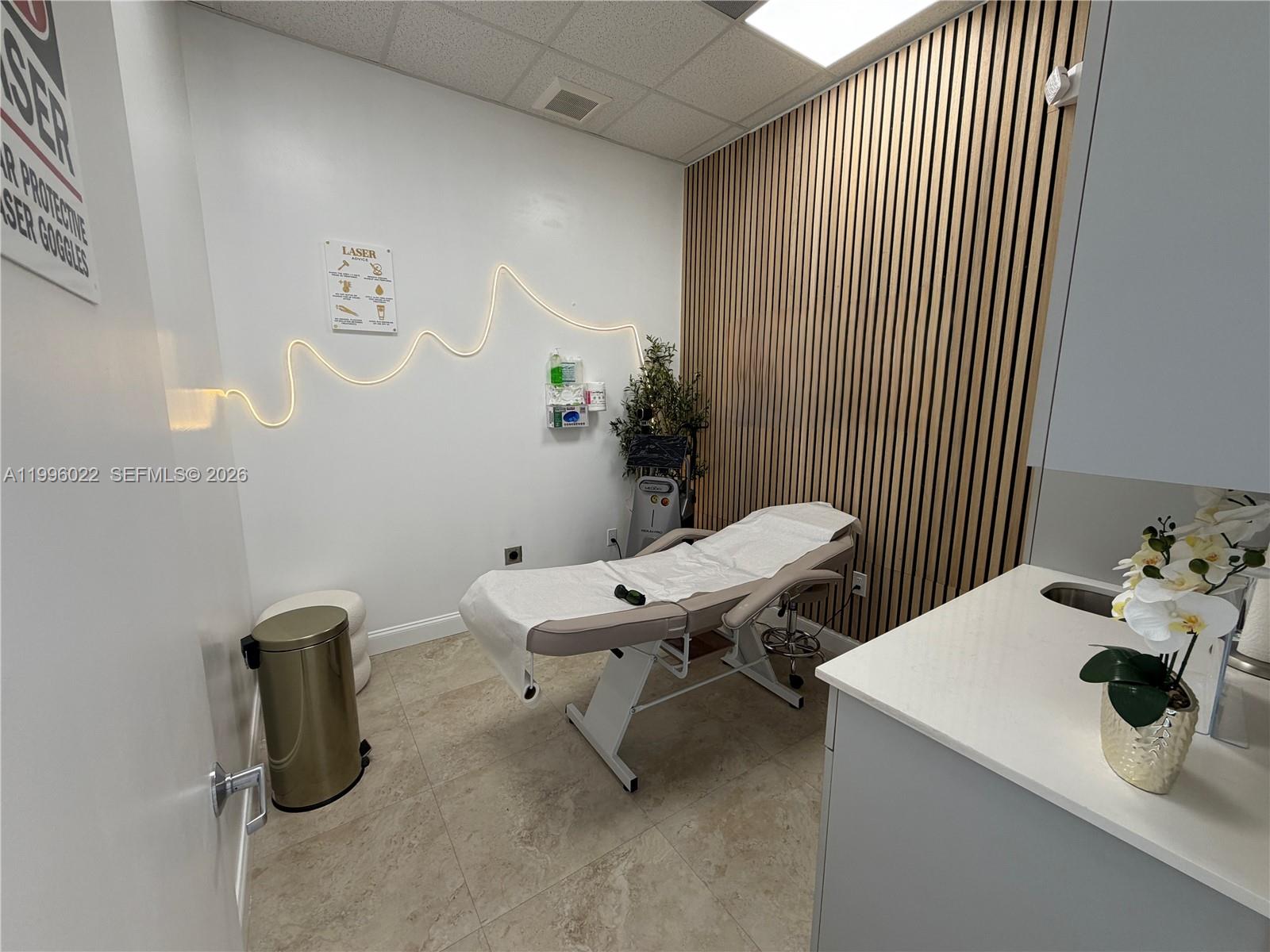 A treatment room features a massage table, wood-slat wall, and a sink area — MED SPA FOR SALE, Miramar FL 33025, MIRAMAR, FL