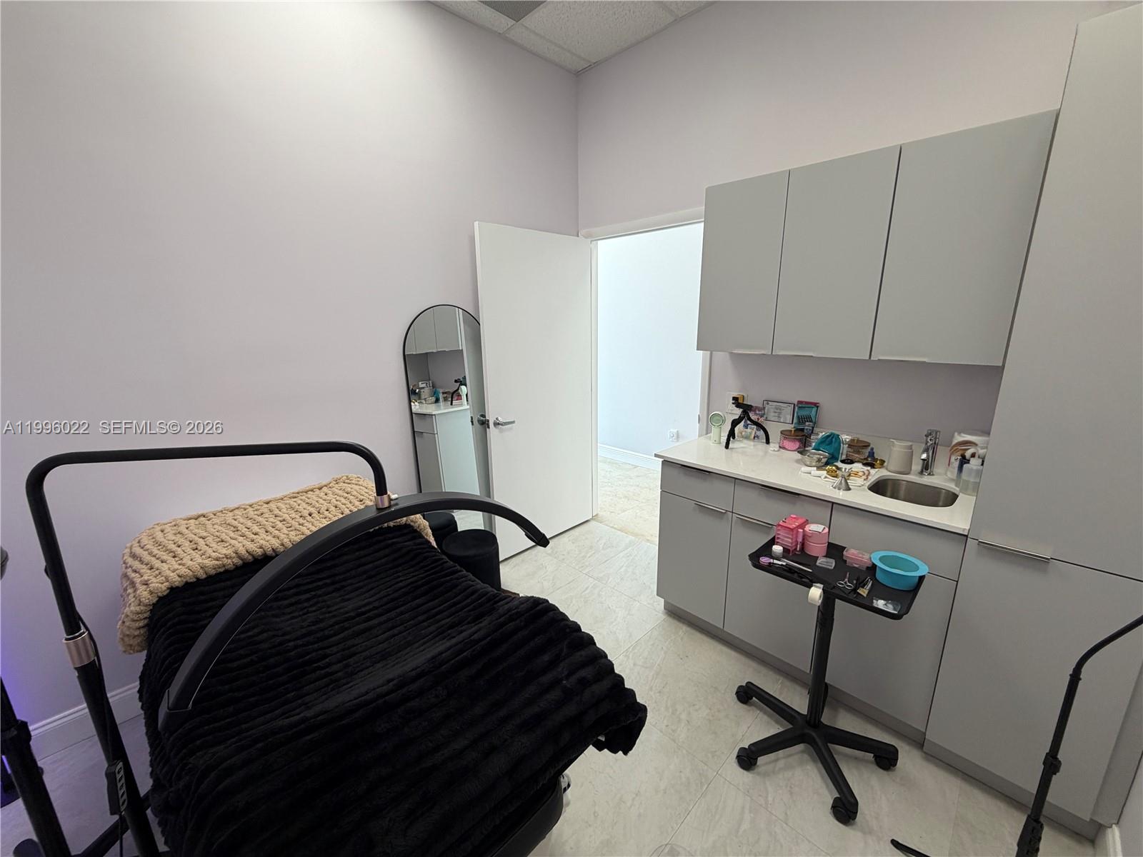 A small treatment room features a massage table, a sink, cabinetry, and a rolling cart — MED SPA FOR SALE, Miramar FL 33025, MIRAMAR, FL