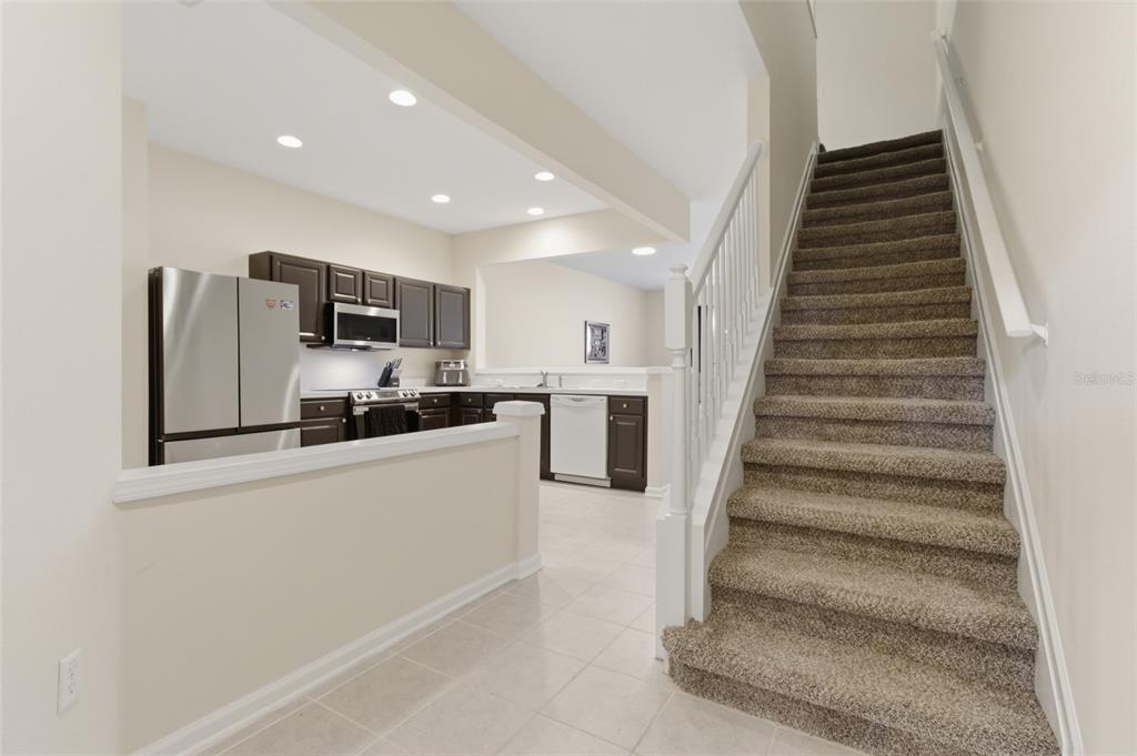 A kitchen with dark cabinets and stainless steel appliances sits beside a carpeted staircase — 26531 CHIMNEY SPIRE LANE, WESLEY CHAPEL, FL