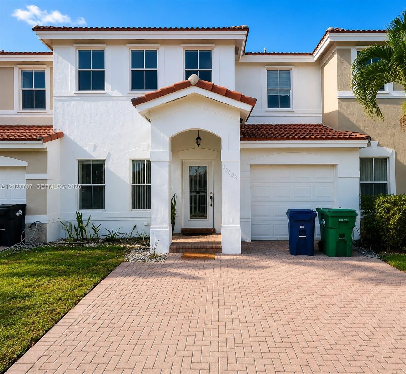 A two-story stucco townhouse with a tiled roof, a paved driveway, and two trash bins — 16628 SW 47th Ter, Miami FL 33185, MIAMI, FL