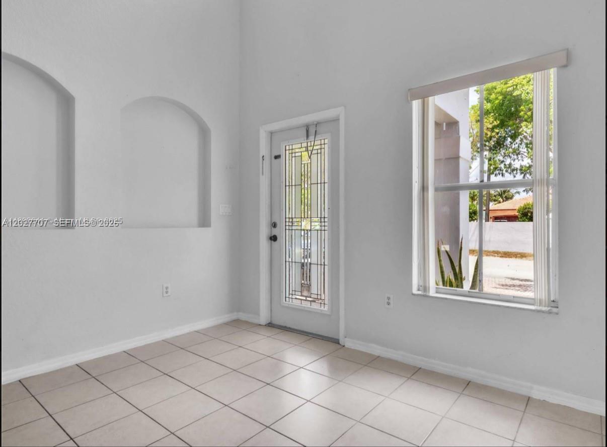 An empty room with light tile flooring, white walls, arched wall niches, and a glass-paneled door — 16628 SW 47th Ter, Miami FL 33185, MIAMI, FL