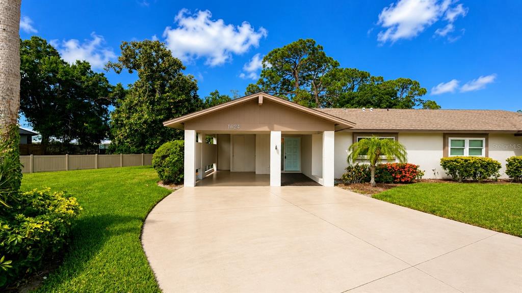 The exterior of a single-story house features a concrete driveway, a covered entryway, and landscaping — 1624 WHITEHEAD DRIVE UNIT 320, SARASOTA, FL