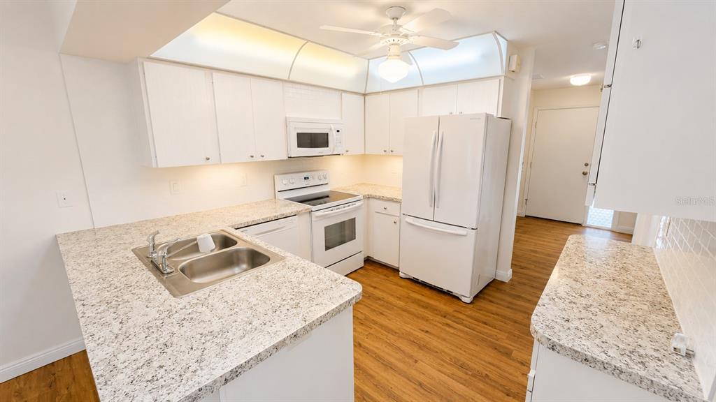A kitchen features white cabinets, granite countertops, stainless steel sink, and white appliances — 1624 WHITEHEAD DRIVE UNIT 320, SARASOTA, FL
