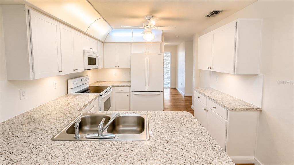 A kitchen features white cabinets, granite countertops, a double sink, and white appliances — 1624 WHITEHEAD DRIVE UNIT 320, SARASOTA, FL