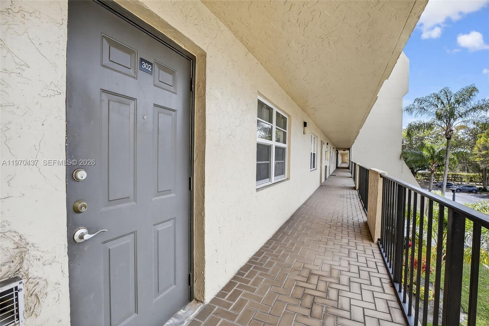 An exterior walkway with a gray door numbered 302 and a black metal railing — 3300 W Rolling Hills Cir # 302, Davie FL 33328, DAVIE, FL