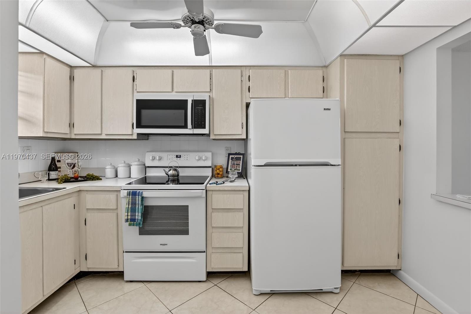 A kitchen features light wood cabinets, white appliances, and a ceiling fan — 3300 W Rolling Hills Cir # 302, Davie FL 33328, DAVIE, FL