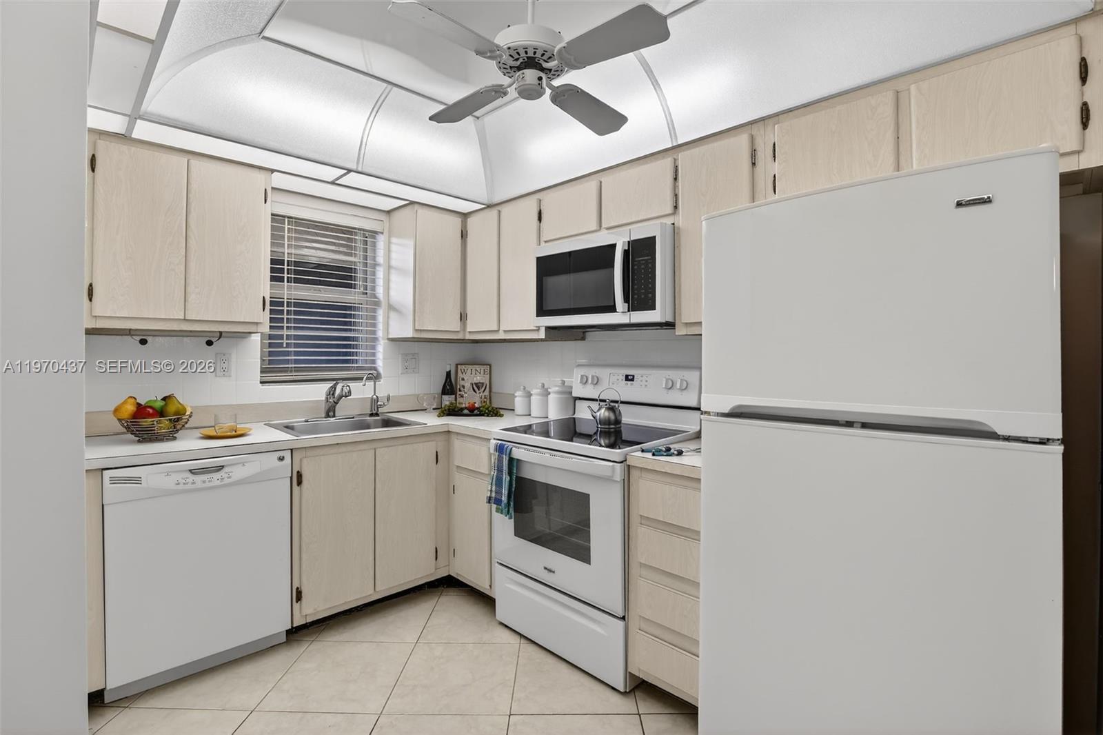 A kitchen features light wood cabinets, white appliances, a ceiling fan, and tile flooring — 3300 W Rolling Hills Cir # 302, Davie FL 33328, DAVIE, FL