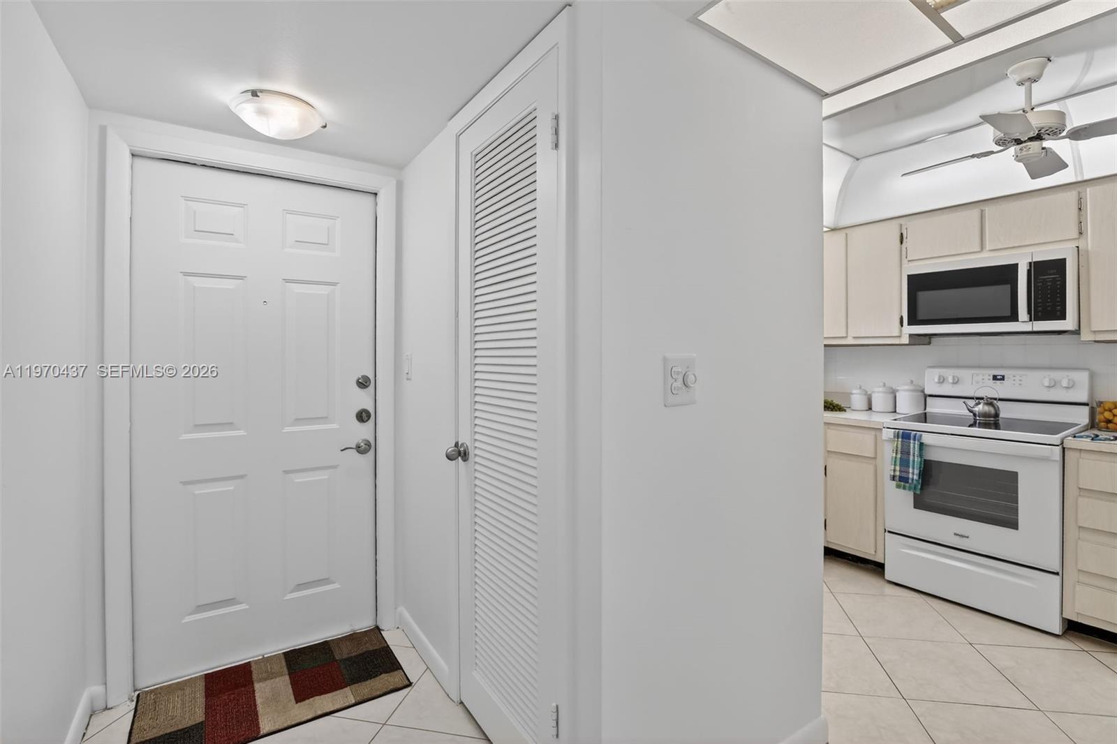 An entryway with a white door and louvered closet leads into a white kitchen — 3300 W Rolling Hills Cir # 302, Davie FL 33328, DAVIE, FL