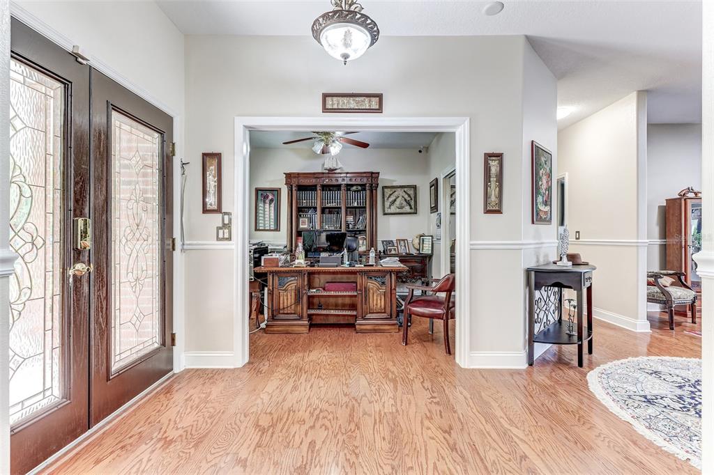 A foyer with hardwood floors leads into a home office featuring a large wooden desk — 9663 GOTHA ROAD, WINDERMERE, FL