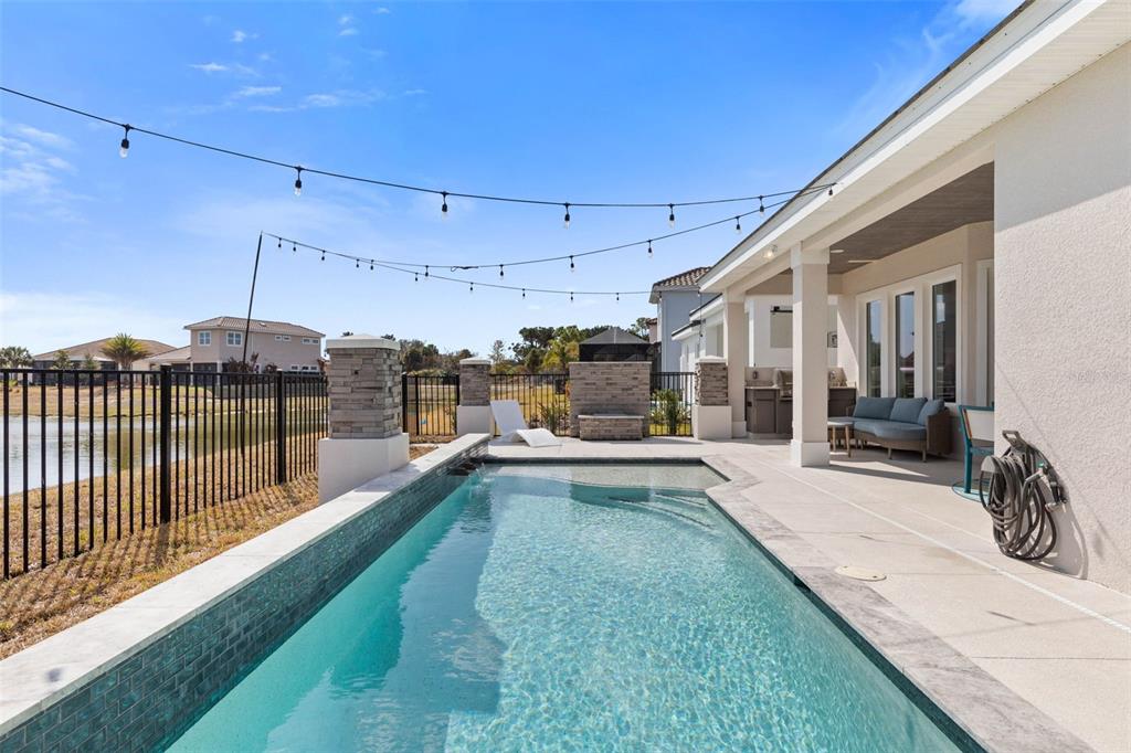 A rectangular swimming pool sits on a patio next to a house with string lights — 122 DEL PALMA DRIVE, PALM COAST, FL