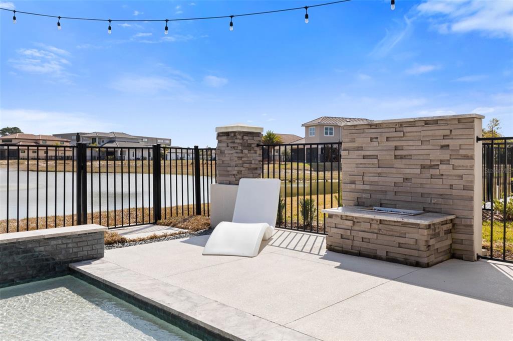 A poolside patio features a lounge chair, a stone fire feature, and a metal fence — 122 DEL PALMA DRIVE, PALM COAST, FL