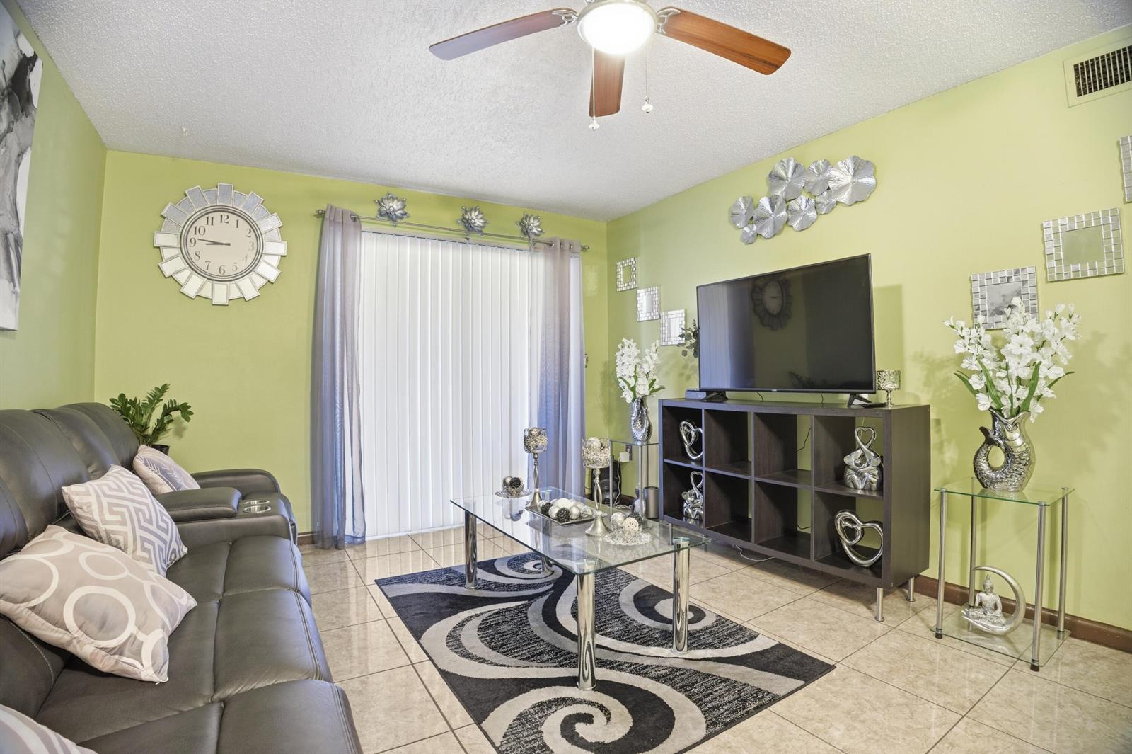 A living room features light green walls, a dark sofa, a glass coffee table, and tile — 6074 Forest Hill Boulevard # 101, West Palm Beach FL 33415, WEST PALM BEACH, FL