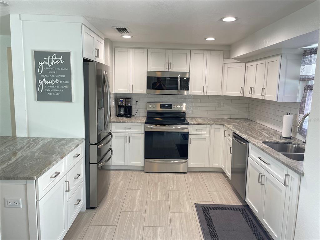 A kitchen features white cabinets, stainless steel appliances, and gray-toned stone countertops — 3410 BAY STREET, SARASOTA, FL
