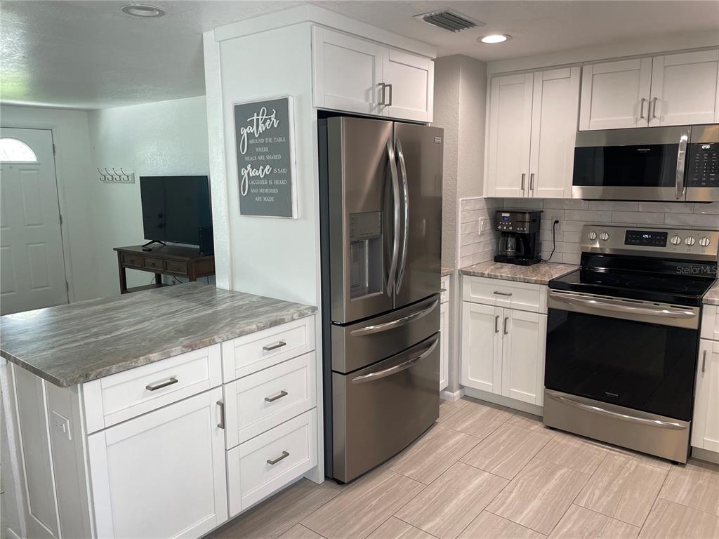 A kitchen features white cabinets, stainless steel appliances, and a gray stone-patterned countertop — 3410 BAY STREET, SARASOTA, FL