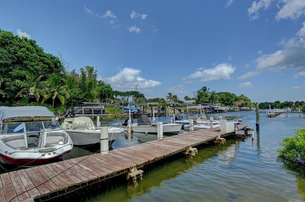 A wooden dock extends into a canal lined with several small boats and lush vegetation — 342 Southwind Drive # 216, North Palm Beach FL 33408, NORTH PALM BEACH, FL