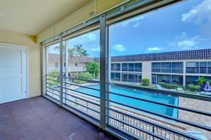 A balcony with a screen enclosure overlooks a swimming pool and a multi-story apartment building — 342 Southwind Drive # 216, North Palm Beach FL 33408, NORTH PALM BEACH, FL