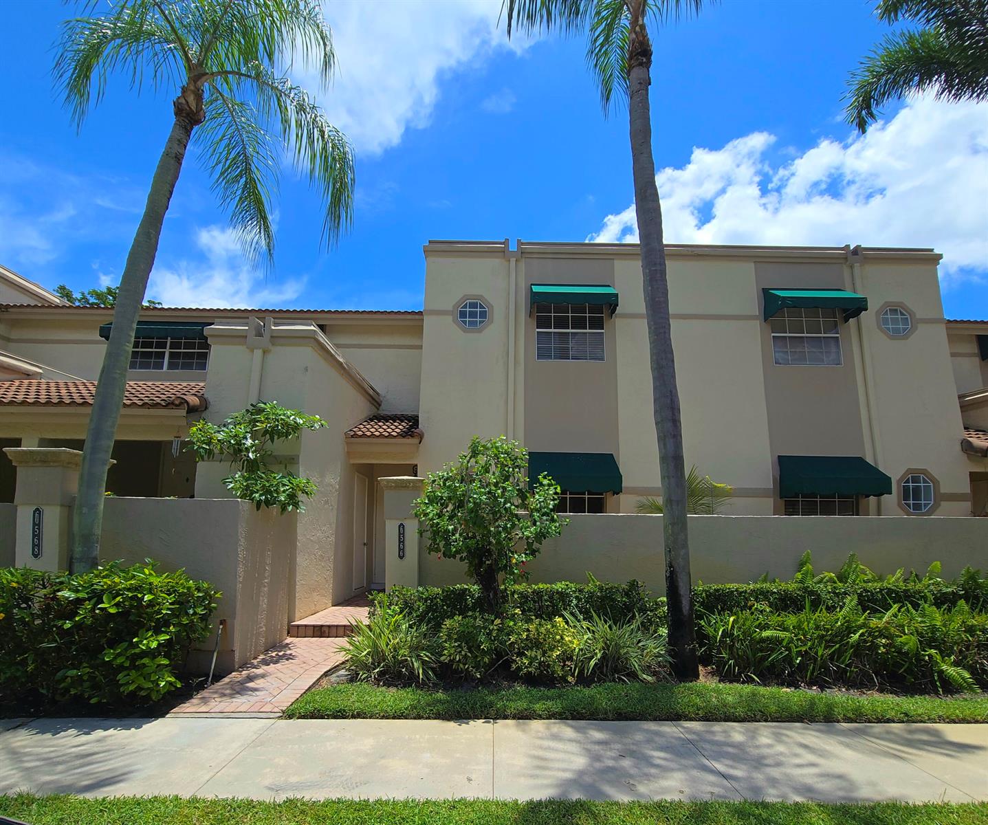 A two-story townhouse exterior features beige stucco walls, green window awnings, and palm trees — 6566 Via Regina # 6566, Boca Raton FL 33433, BOCA RATON, FL