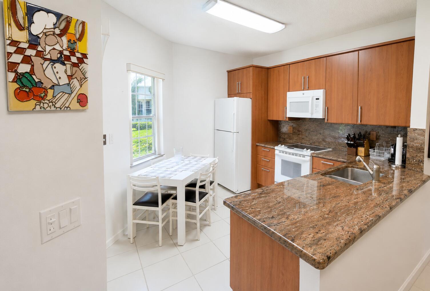 A kitchen features wood cabinets, granite countertops, white appliances, and a small dining area — 6566 Via Regina # 6566, Boca Raton FL 33433, BOCA RATON, FL