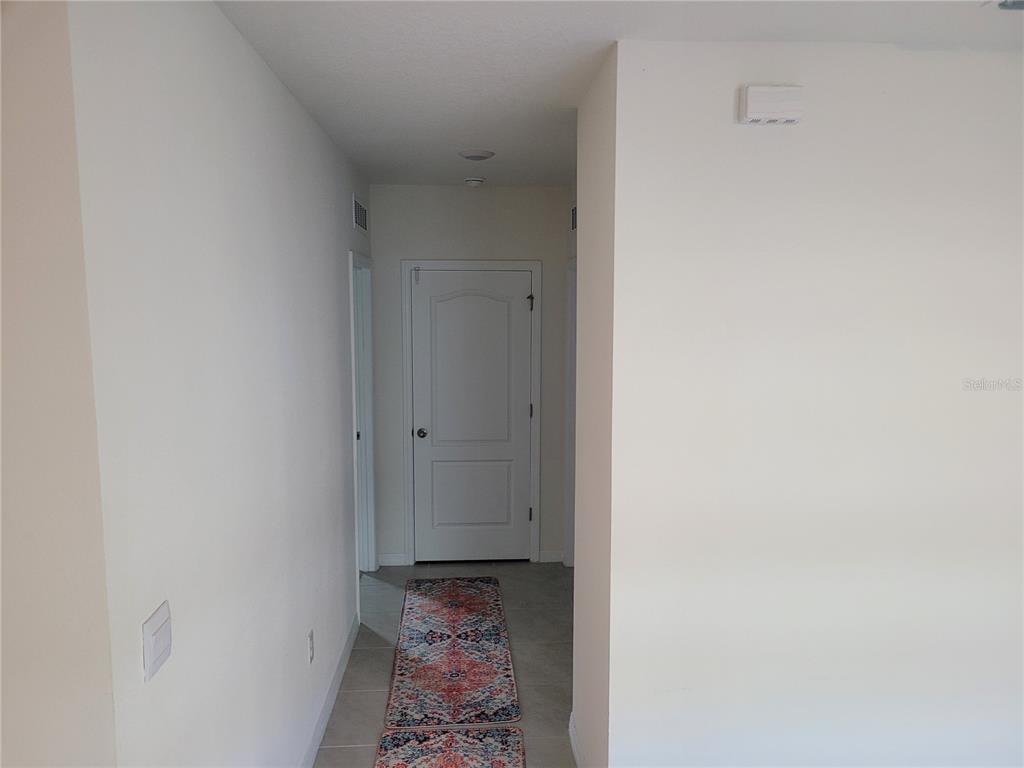 A hallway with light-colored walls, tile flooring, and a white door at the end — 2763 REDDISH EGRET BEND, HARMONY, FL